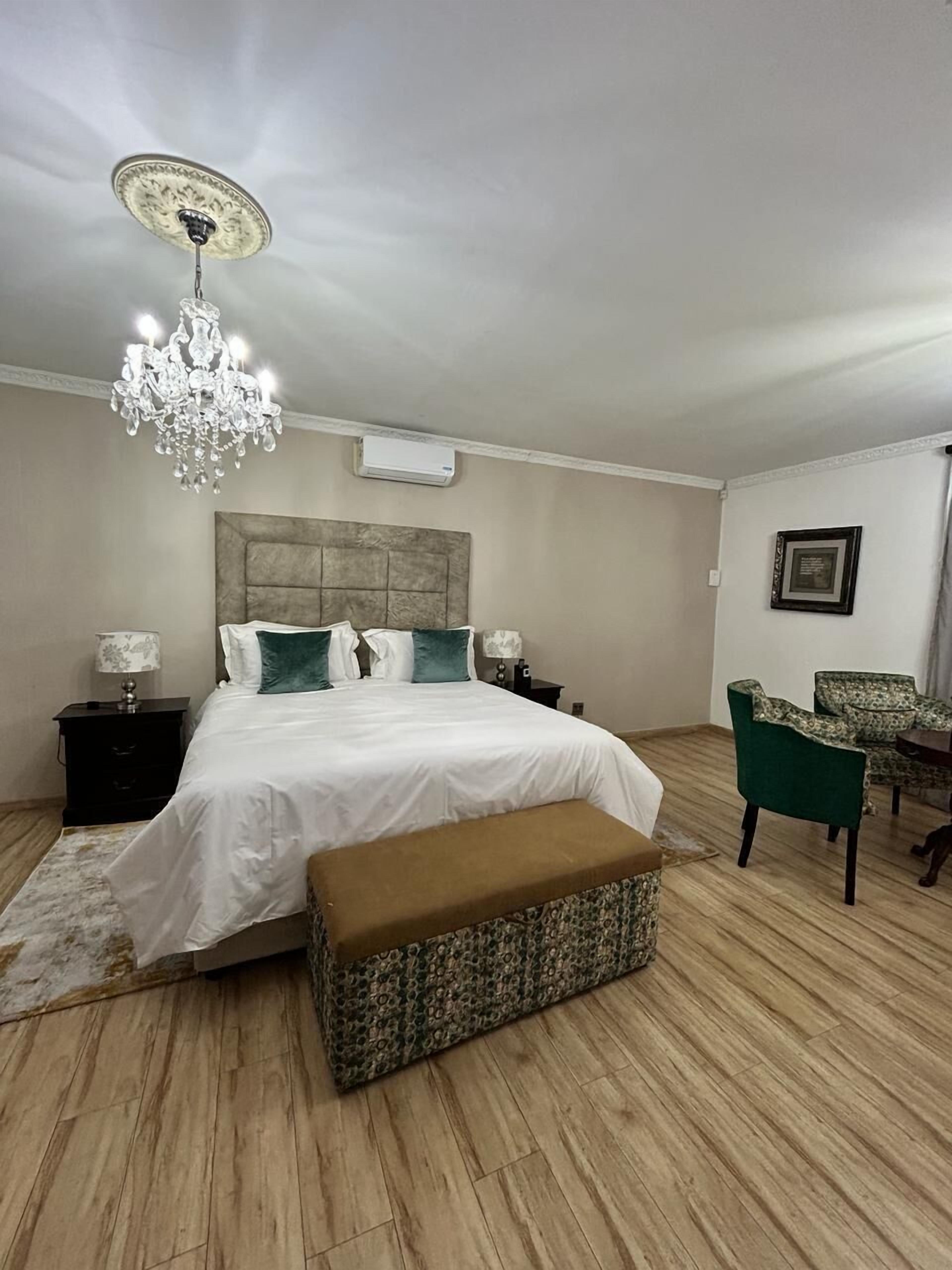 Un dormitorio con una cama grande, una banca, una silla, una araña y un aire acondicionado de pared.
