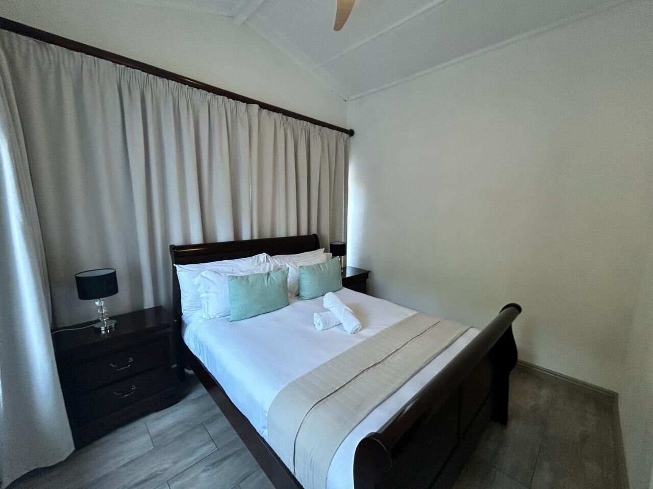 A neatly made bed with white linens, a wooden headboard, and a bedside table with a lamp.