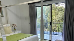 Een slaapkamer met een hemelbed, een bankje, een nachtkastje met lamp en uitzicht op de natuur via een schuifdeur.
