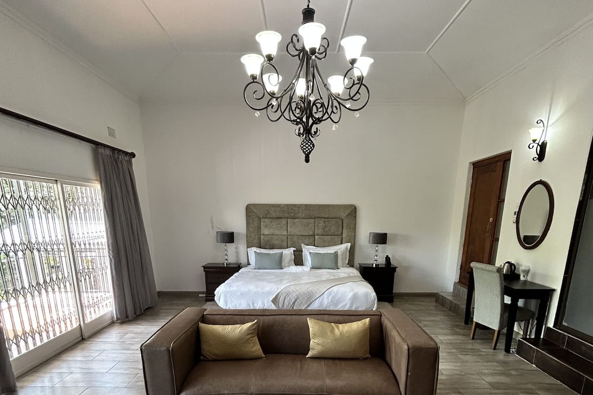 Een ruime slaapkamer met een groot bed, een kroonluchter, een bank en een bureau.