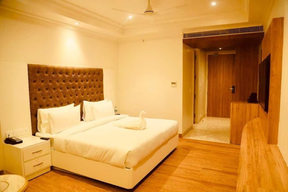 Habitació d'hotel amb un llit gran, un capçal, una taula de nit, un comandament a distància i un terra de fusta.