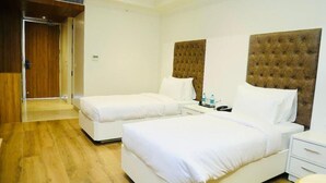 Una habitación de hotel con dos camas, suelo de madera y puerta de madera.