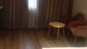 Una habitación de hotel con cama, una mesa redonda, dos sillas y un ventanal con cortinas.