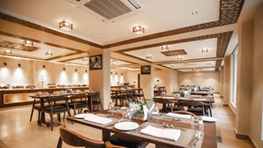 A spacious dining area with multiple tables and chairs, a central serving station, and a modern ceiling design with recessed lighting. - The Sarai (Srinagar)