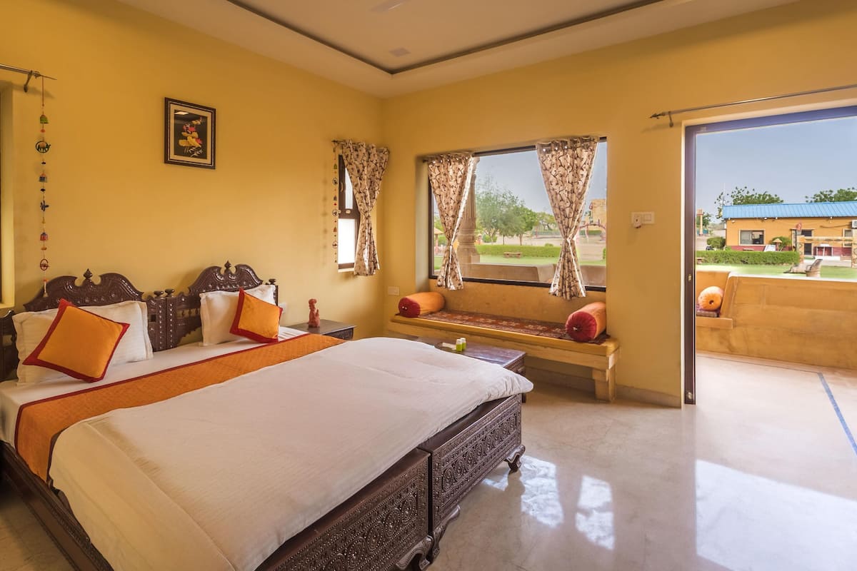 A hotel room with a large bed, a bench with cushions, a ceiling fan, and a view of the outside.