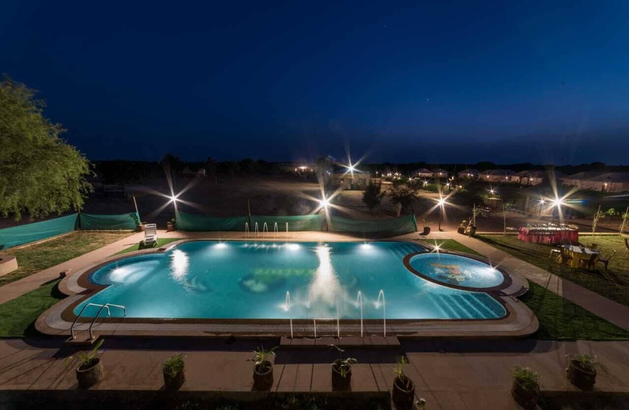 Una piscina con múltiples chorros, rodeada por una terraza con plantas en macetas y vistas a edificios lejanos.