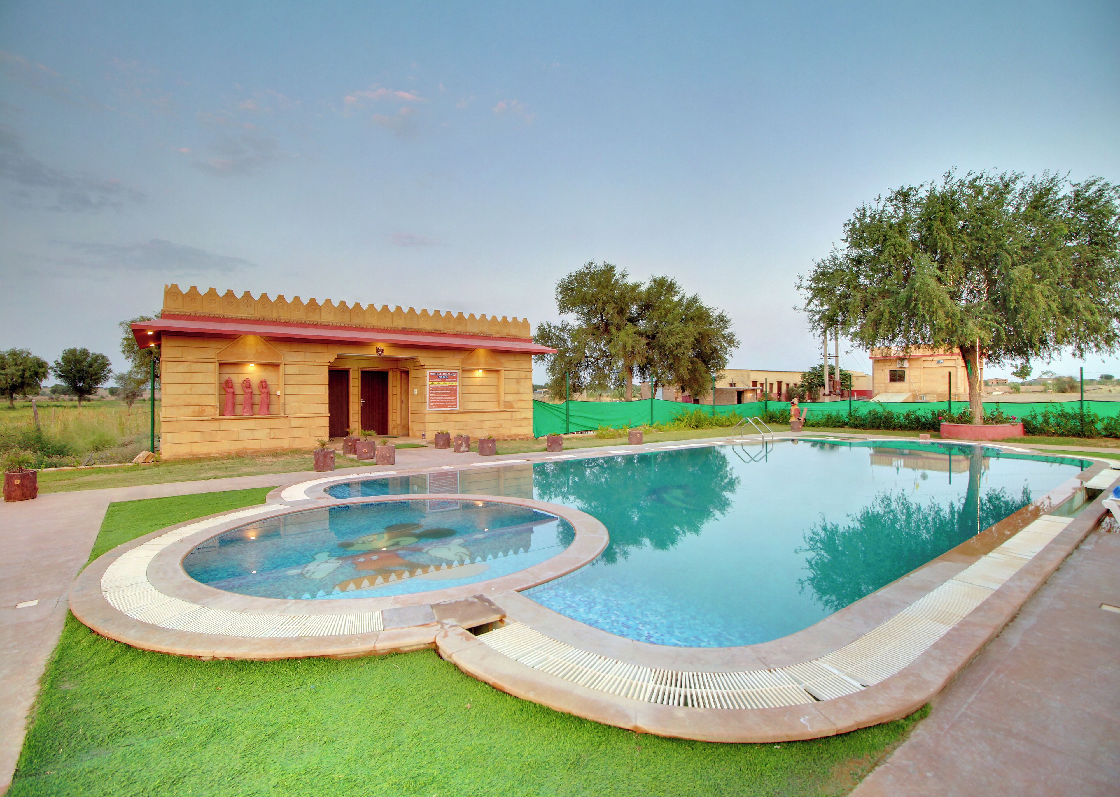 A swimming pool with a surrounding deck, a wooden building with a red roof, and a green fence.