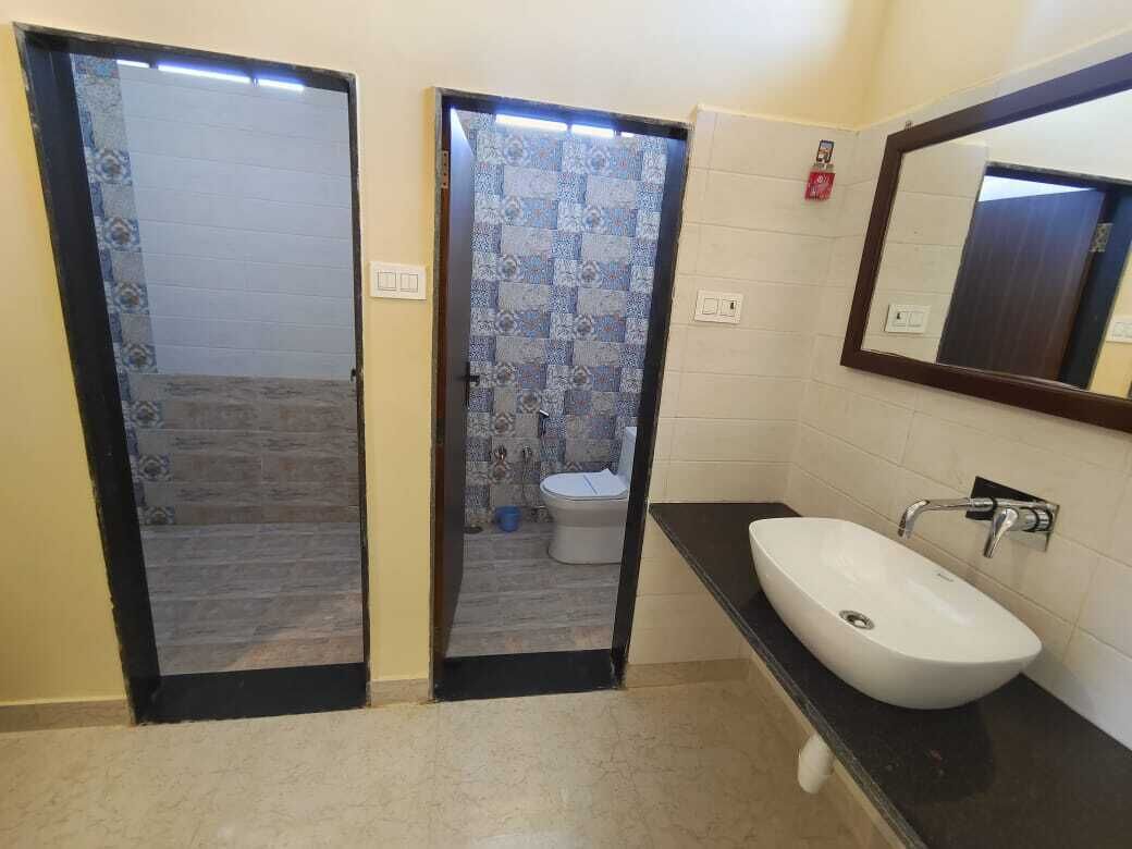 A bathroom with a white sink, a mirror, and a toilet visible through a glass door.