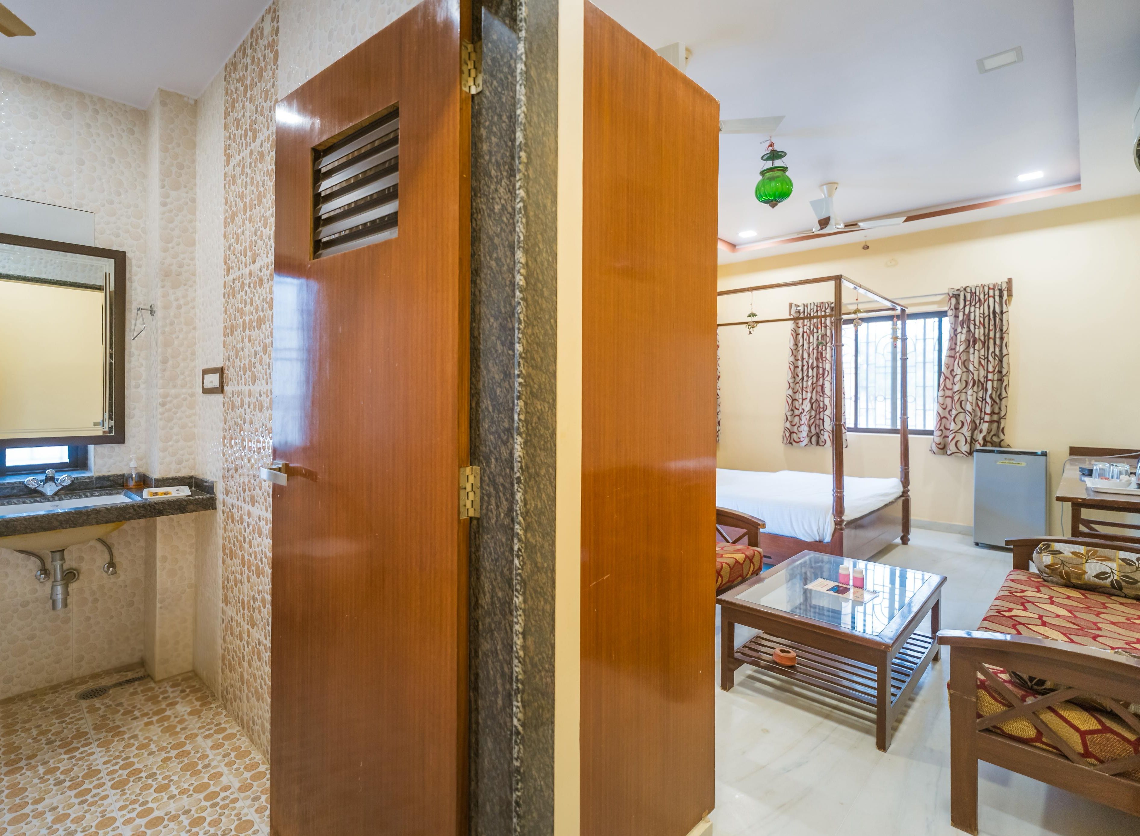 Quarto de hotel com banheiro, cama, escrivaninha e janela com cortinas.