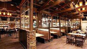 Un restaurante con vigas de madera, pilares de piedra y diferentes opciones de asientos, incluyendo cabinas y mesas.