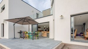 Un patio moderno al aire libre con una mesa de comedor y sillas, un paraguas grande y una cubierta de madera.