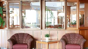 A lobby with two patterned armchairs, a small table with a potted plant, and a large window with a view of outdoor seating. - B&B Hotel Gotha-hbf (Gotha)