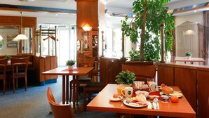 A restaurant with wooden furniture, a large plant, and a breakfast spread on the table. - B&B Hotel Gotha-hbf (Gotha)