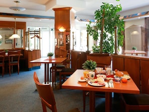 A restaurant with wooden furniture, a large plant, and a breakfast spread on the table.