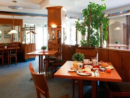 A restaurant with wooden furniture, a large plant, and a breakfast spread on the table.