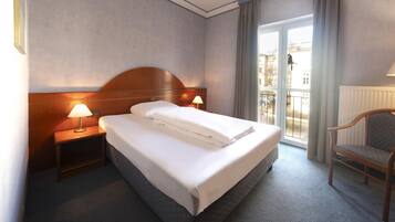 A hotel room with a large bed, two bedside lamps, a chair, and a view of the city through the window.