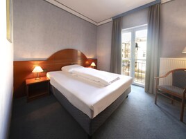 Habitación de hotel con una cama grande, dos lámparas de noche, una silla y vista a la ciudad desde la ventana.