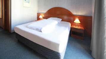 Una habitación de hotel con una cama grande, dos mesitas de noche con lámparas, un cabecero de madera y piso alfombrado.