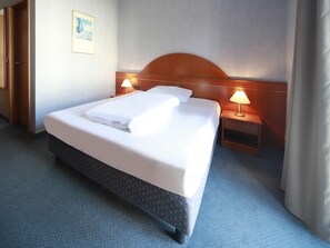 A hotel room with a large bed, two bedside tables with lamps, a wooden headboard, and a carpeted floor.