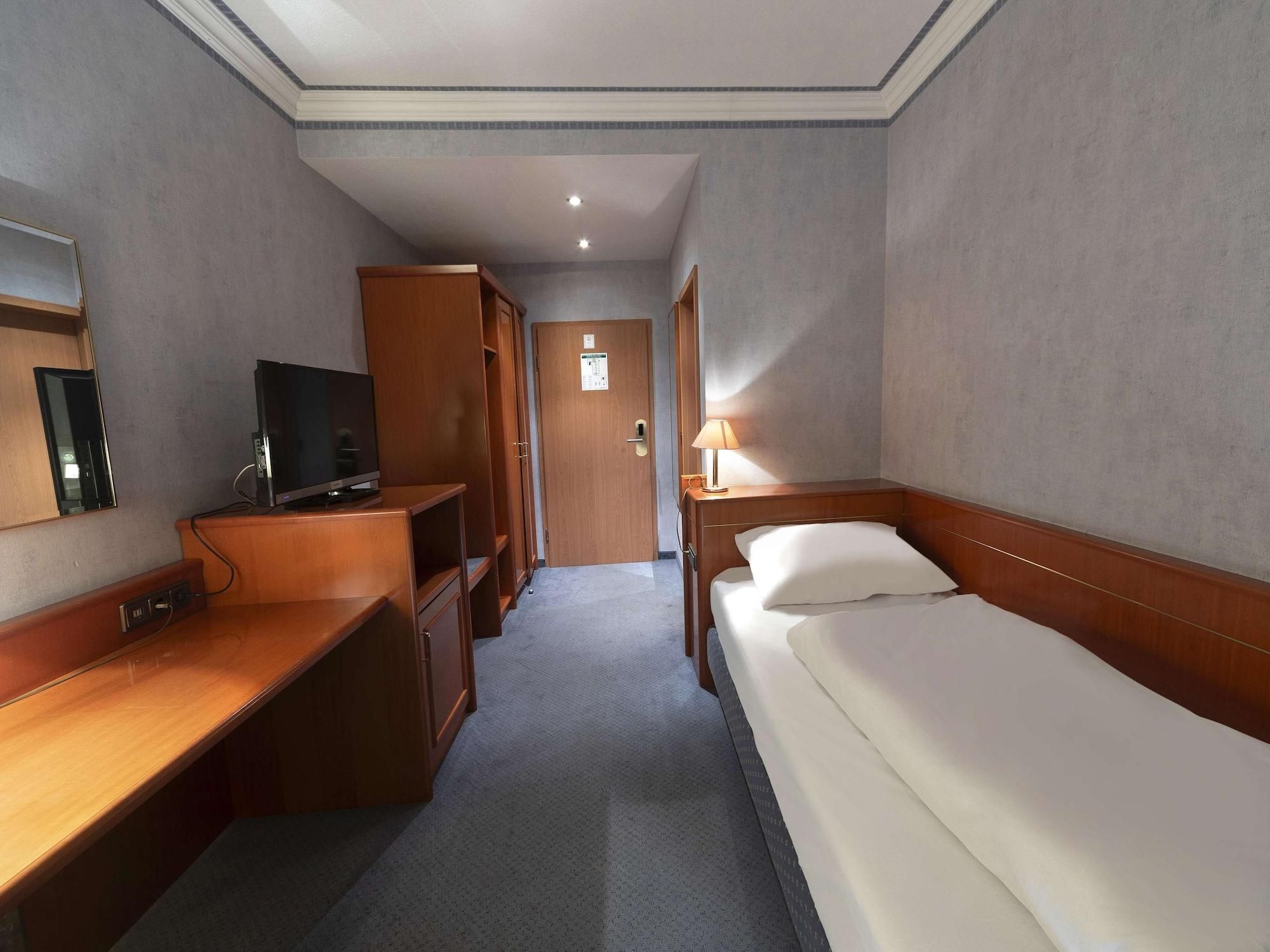 Una habitación de hotel con cama, escritorio, televisor y armario.