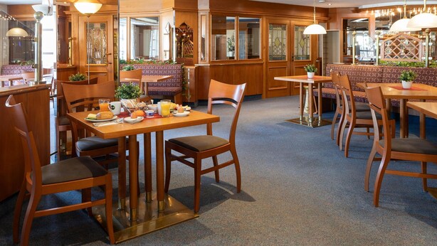 A restaurant with wooden furniture, a high ceiling, and a cozy atmosphere. - B&B Hotel Gotha-hbf (Gotha)