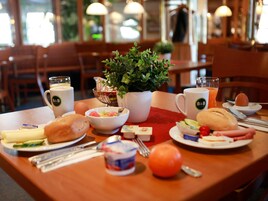 Una mesa de desayuno con diversas opciones de comida, una planta y dos tazas con la marca B&B.