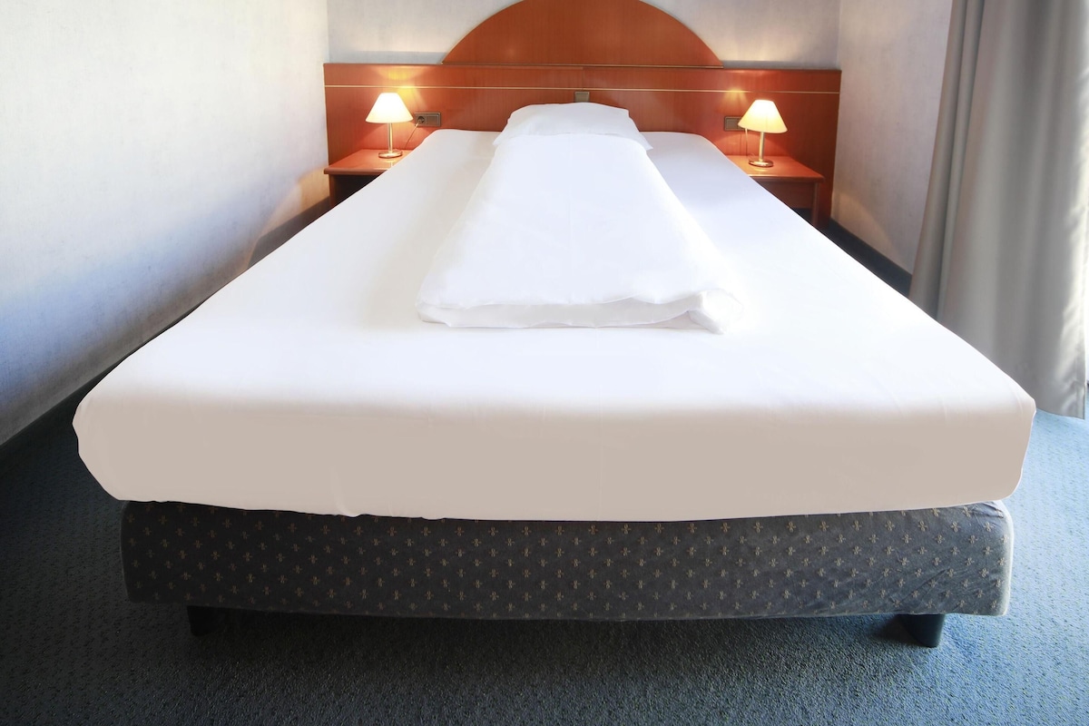 A hotel room with a single bed, two bedside lamps, and a headboard.