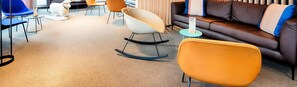 Una sala de estar moderna con un sofá de cuero marrón, sillones naranjas y una mecedora blanca.