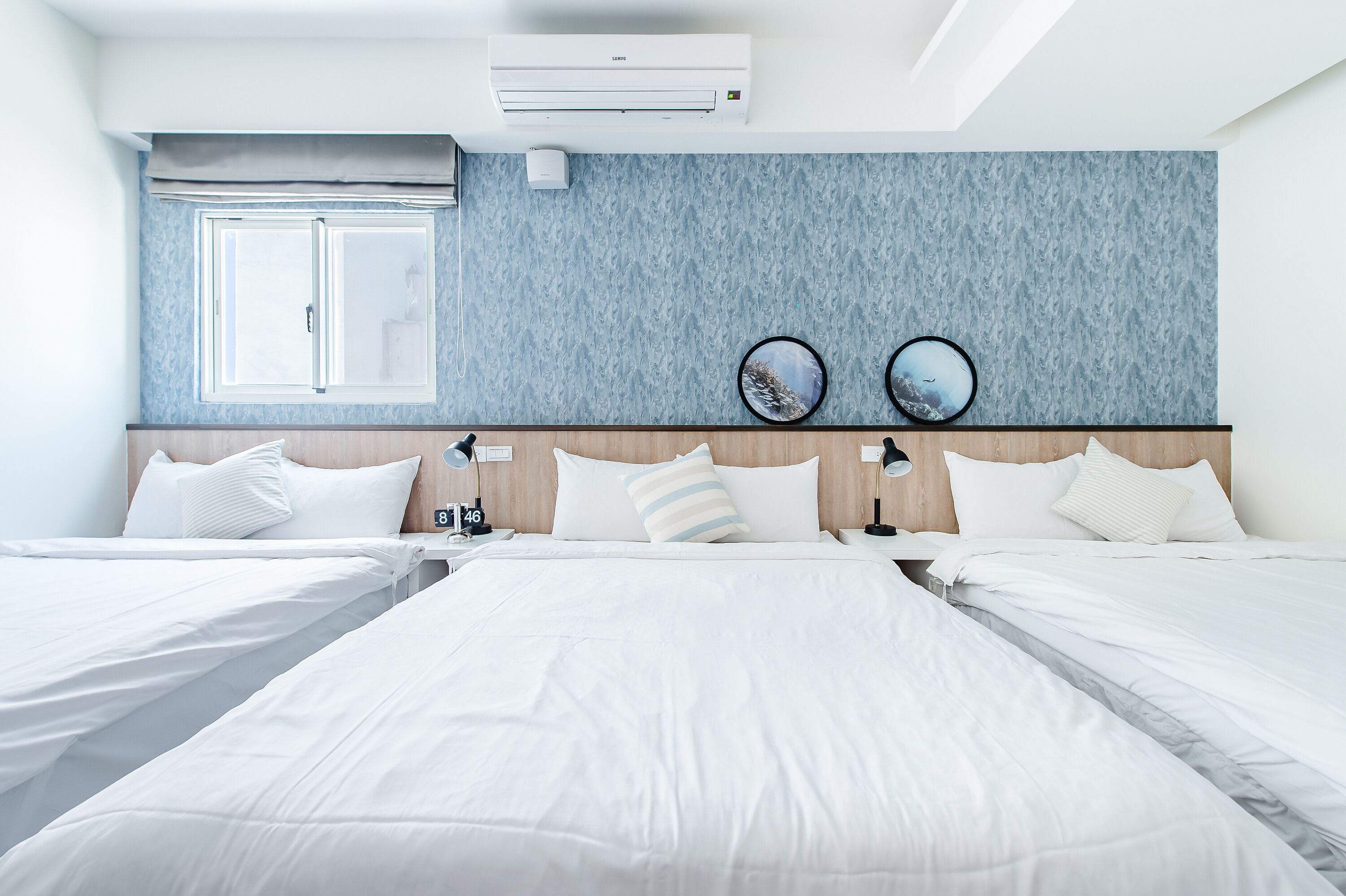Een hotelkamer met twee bedden, een groot raam, een airconditioning en een klok aan de muur.