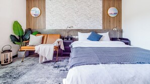 Une chambre à coucher moderne avec un lit, des tables de chevet, une petite table, une chaise, une plante en pot et un miroir fixé au mur.