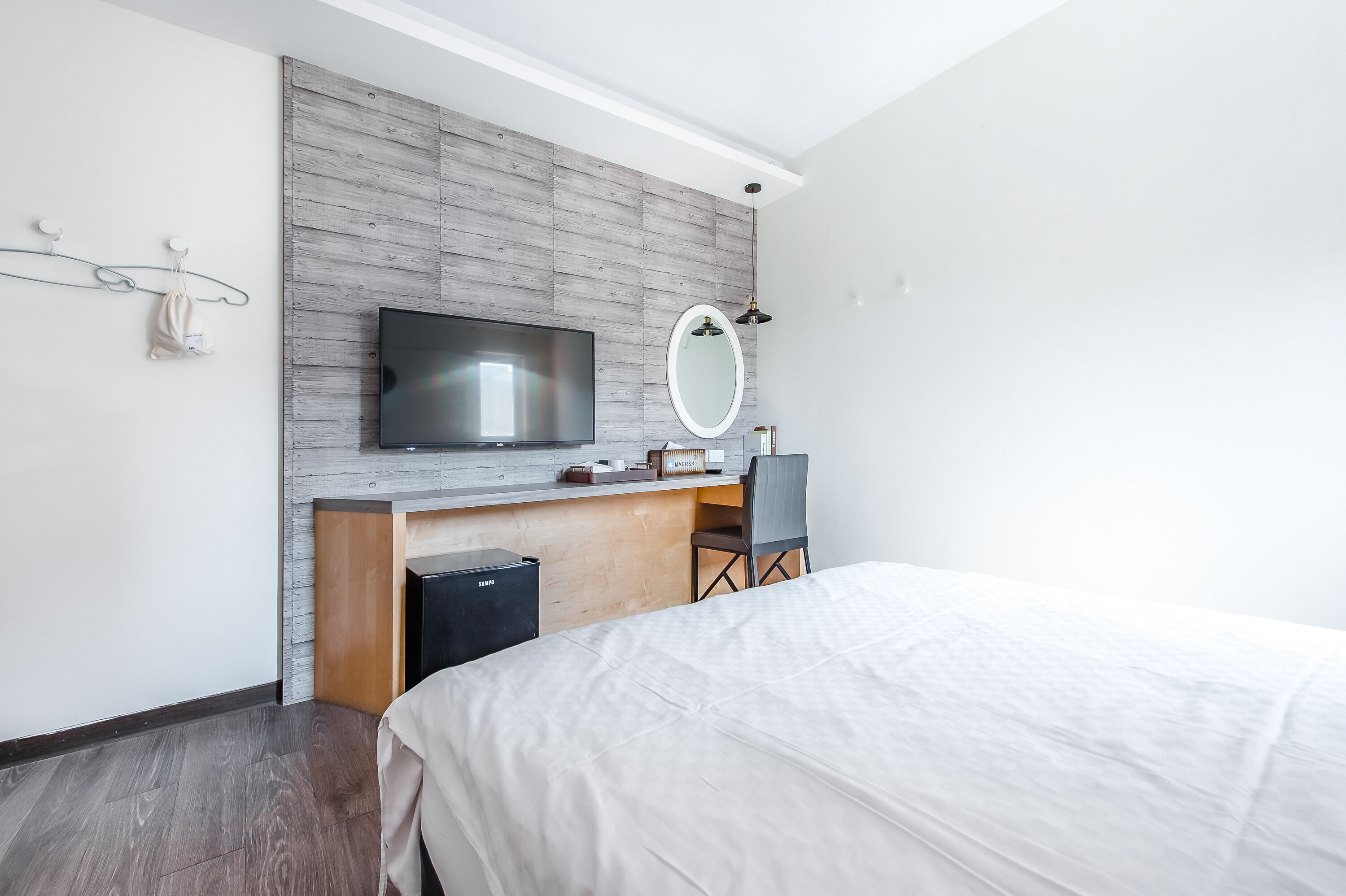 A modern hotel room with a large bed, a desk with a chair, a television, and a mirror.