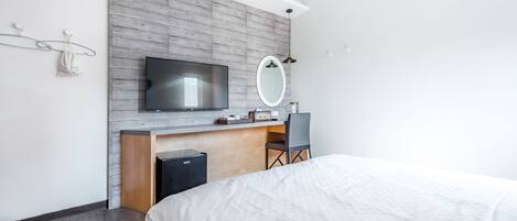 A modern hotel room with a large bed, a desk with a chair, a television, and a mirror.