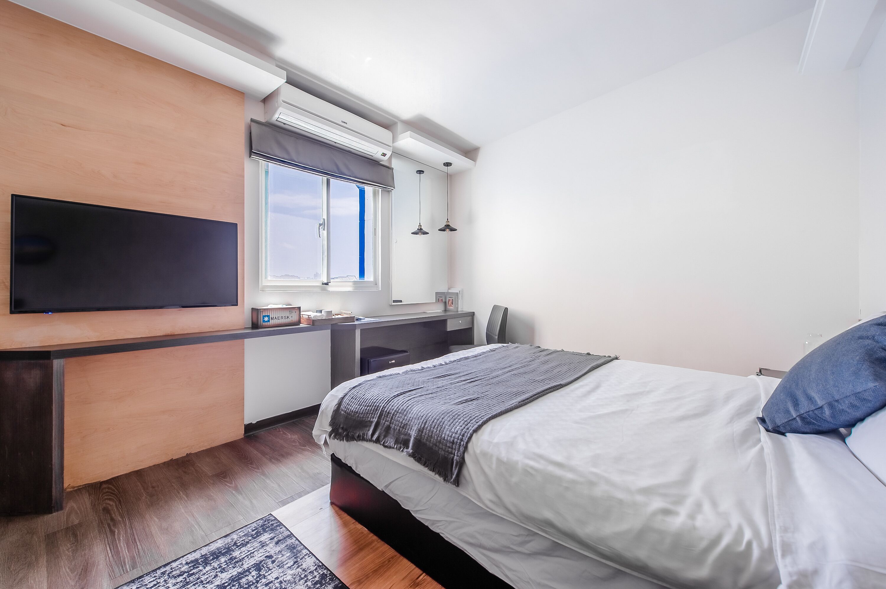 Un dormitorio moderno con una cama grande, un televisor de pantalla plana en la pared, un escritorio con silla y una ventana con persianas.