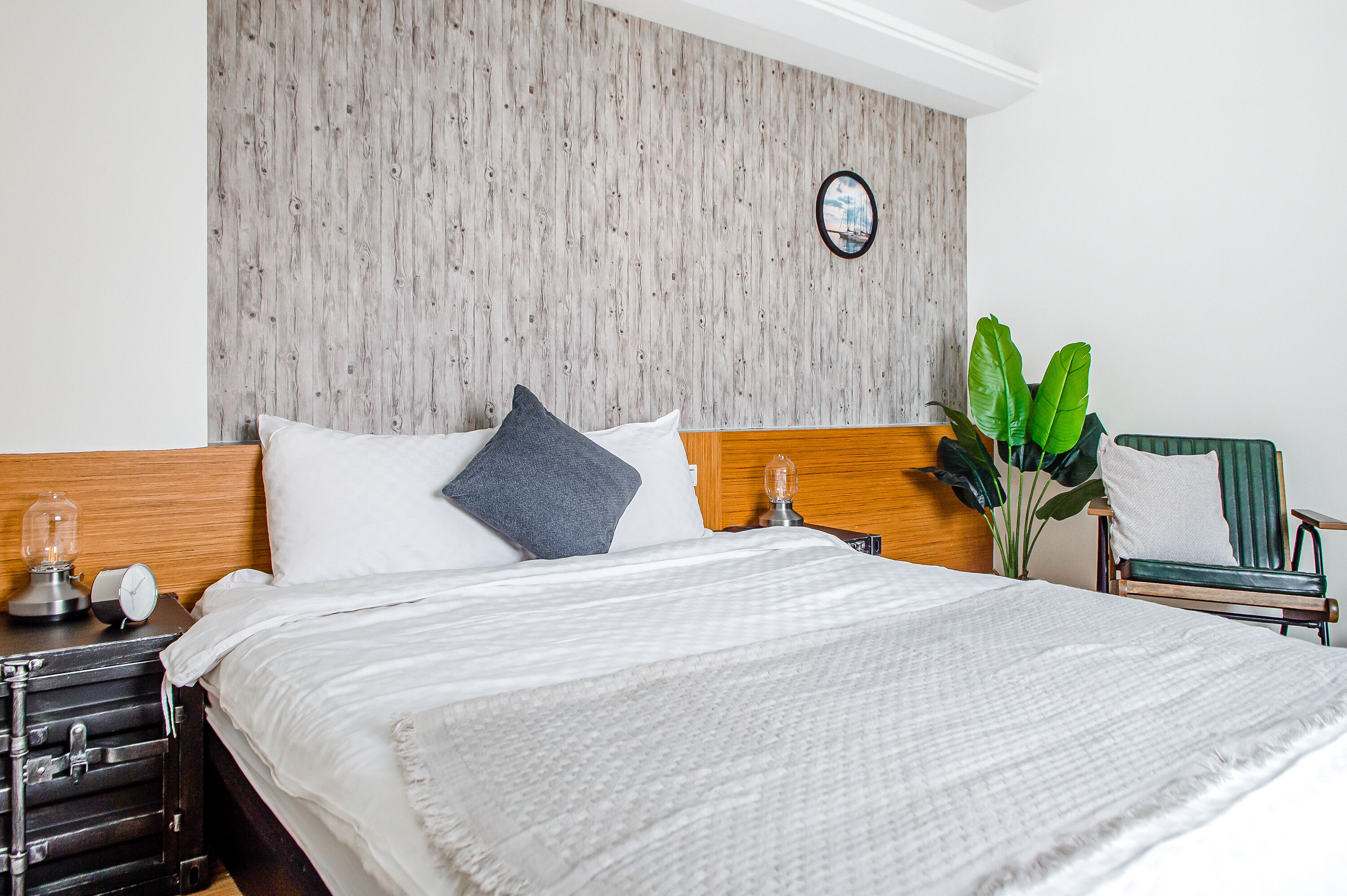 Una cama bien tendida con un cabecero de madera, una mesita de noche con una lámpara y una planta en maceta.