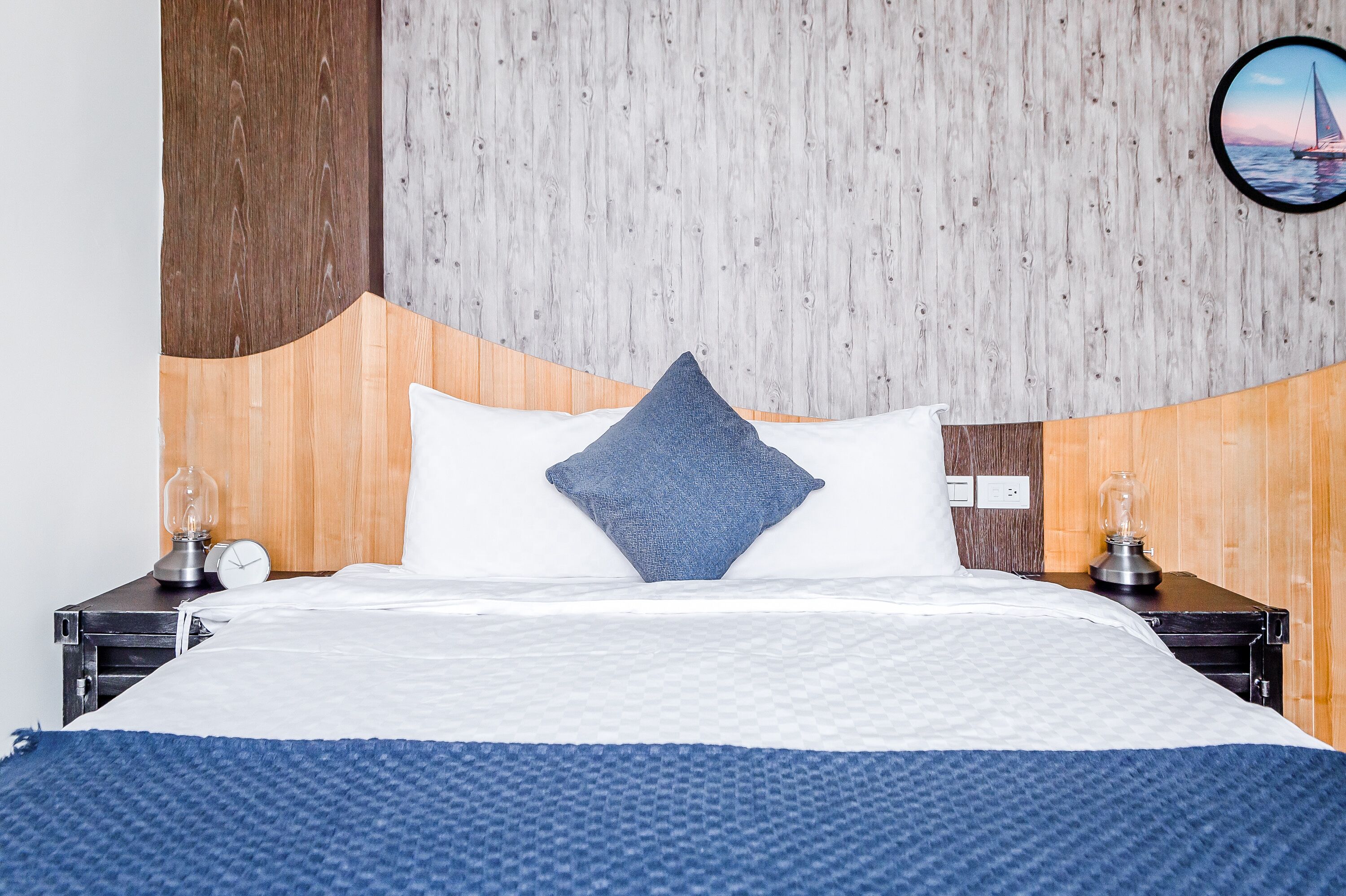A neatly made bed with a blue and white color scheme, wooden headboard, and a round wall clock.
