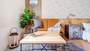 Une chambre moderne avec un canapé en bois, une petite table, une plante en pot, une lanterne en métal et un coffre-fort.