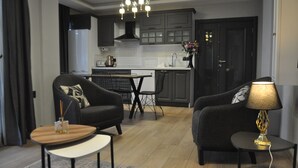 Un salon moderne avec un canapé, une table basse et une lampe. On aperçoit à l’arrière un coin cuisine avec des placards et un évier.