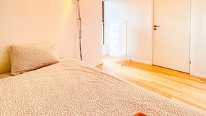 Une chambre à coucher avec une couvre-lit à motifs, un lampadaire et une porte donnant sur une autre pièce.