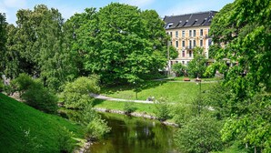 Un parc paisible avec un étang, une végétation luxuriante et un bâtiment historique en arrière-plan.