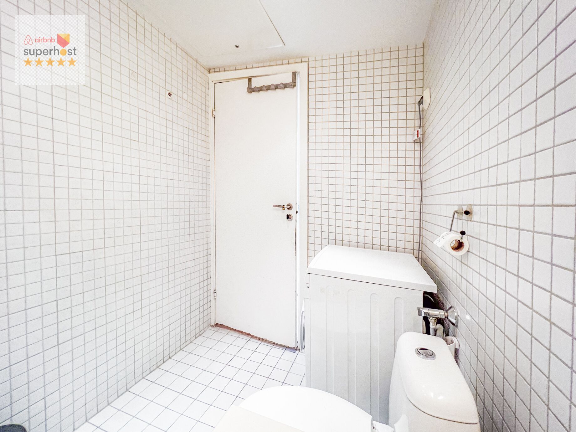 A small, tiled bathroom with a toilet, bidet, and a door leading to another room.