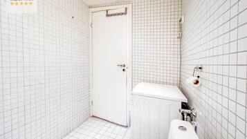 A small, tiled bathroom with a toilet, bidet, and a door leading to another room.
