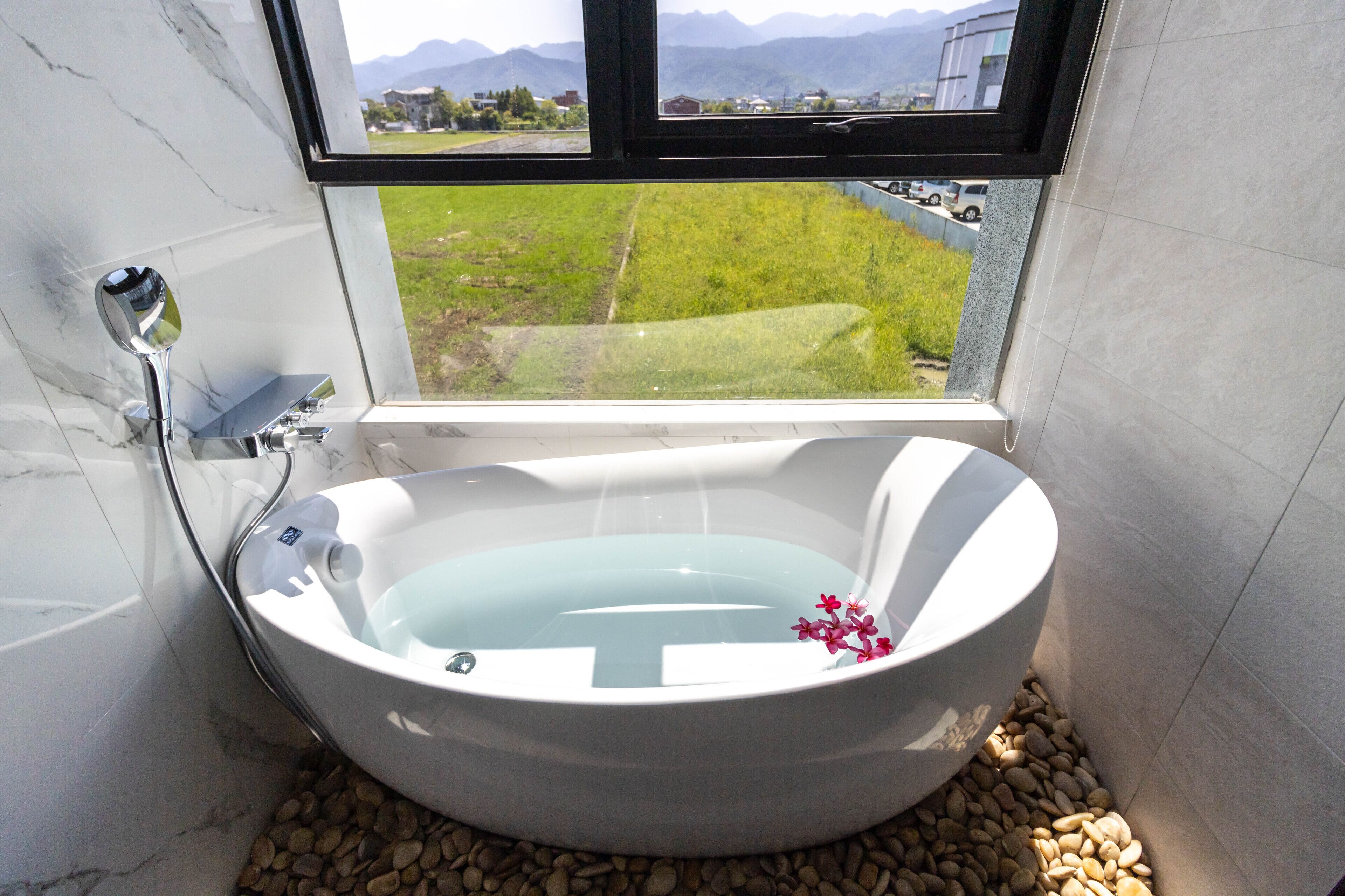 Un baño moderno con una bañera independiente, un ventanal con vistas a un paisaje verde y una pared de mármol.