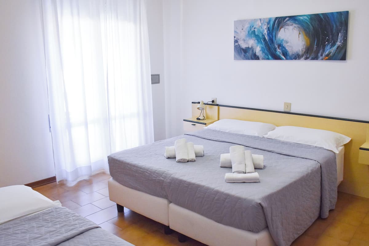 A hotel room with a bed, a nightstand, a painting, and a window with curtains.