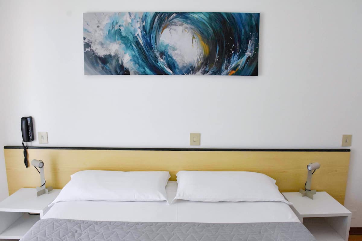 A hotel room with a bed, two bedside tables, a wall-mounted phone, and a painting.