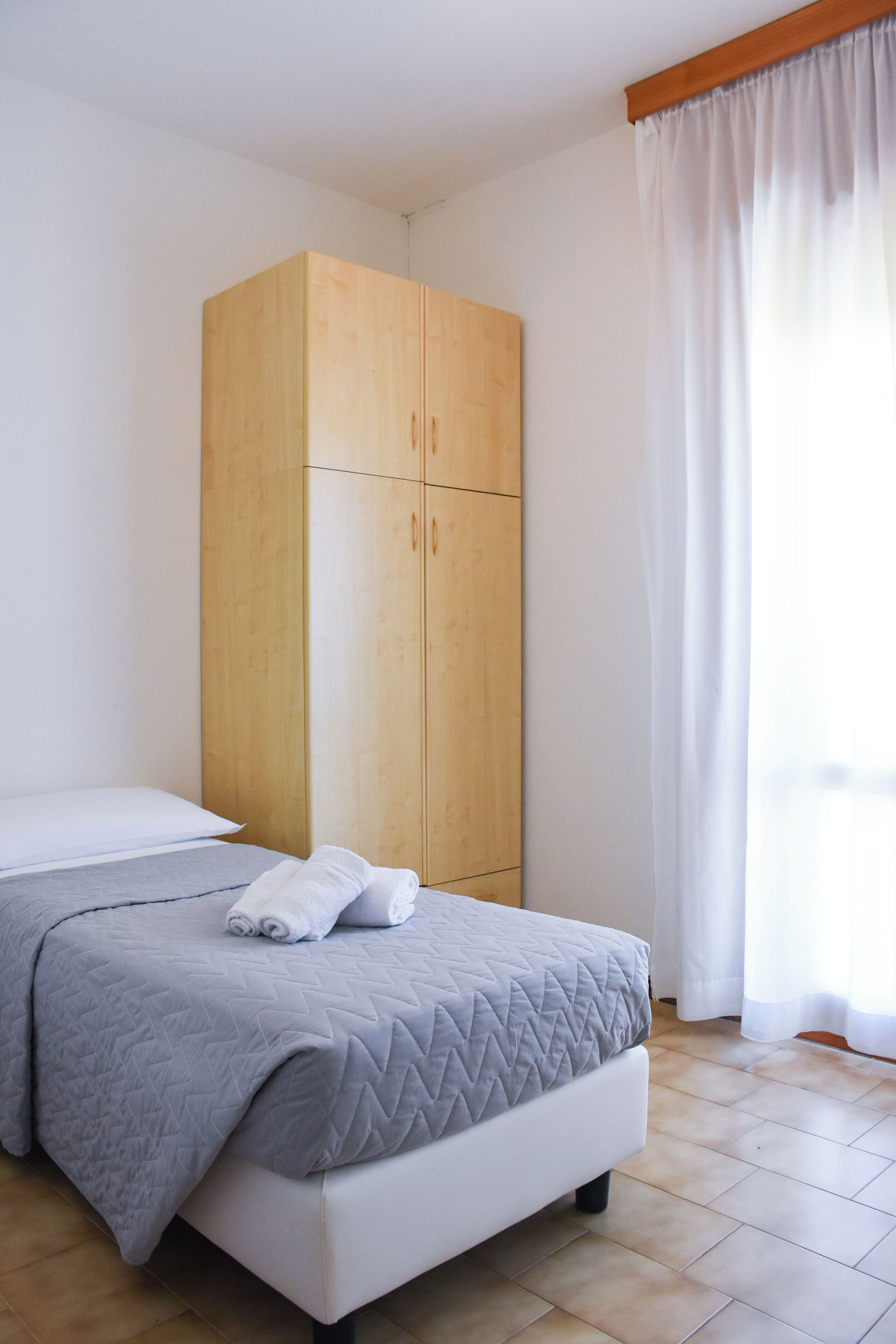 Quarto com cama, guarda-roupa e janela com cortinas.