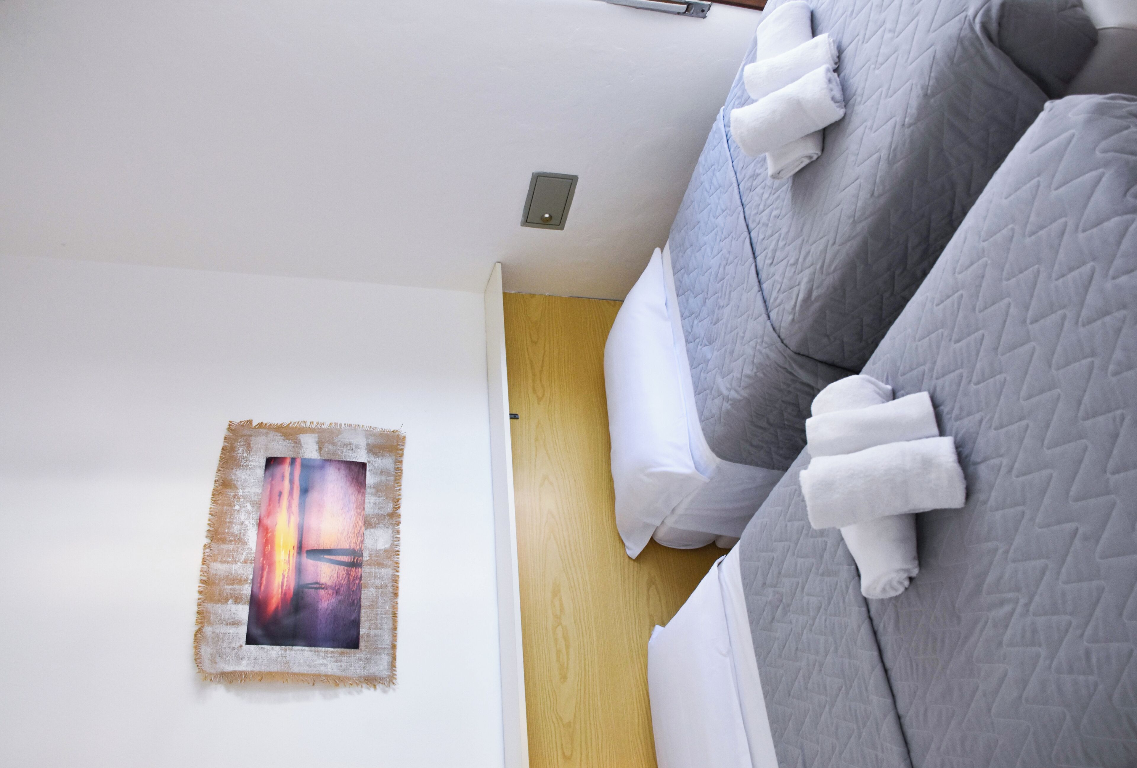 A bedroom with a bed, pillows, a wall-mounted picture, and a wooden floor.