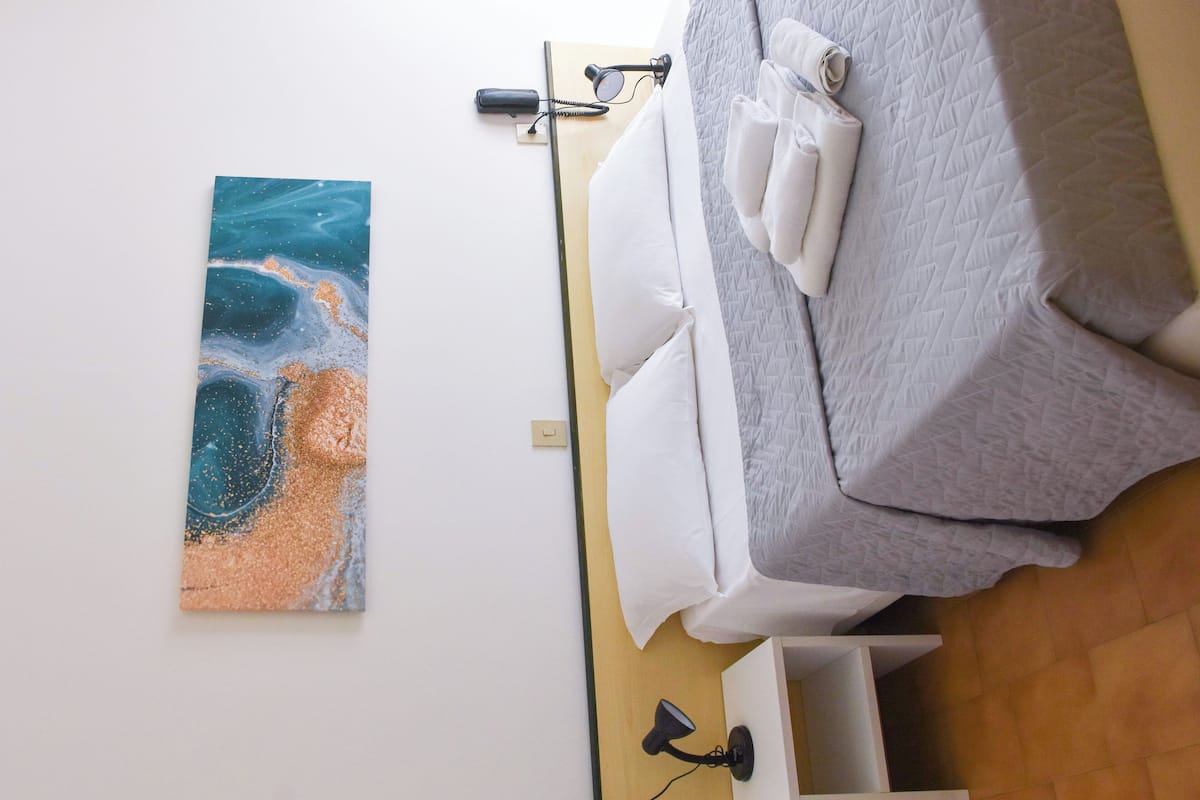 A room with a bed, a nightstand, a wall-mounted lamp, and a painting.