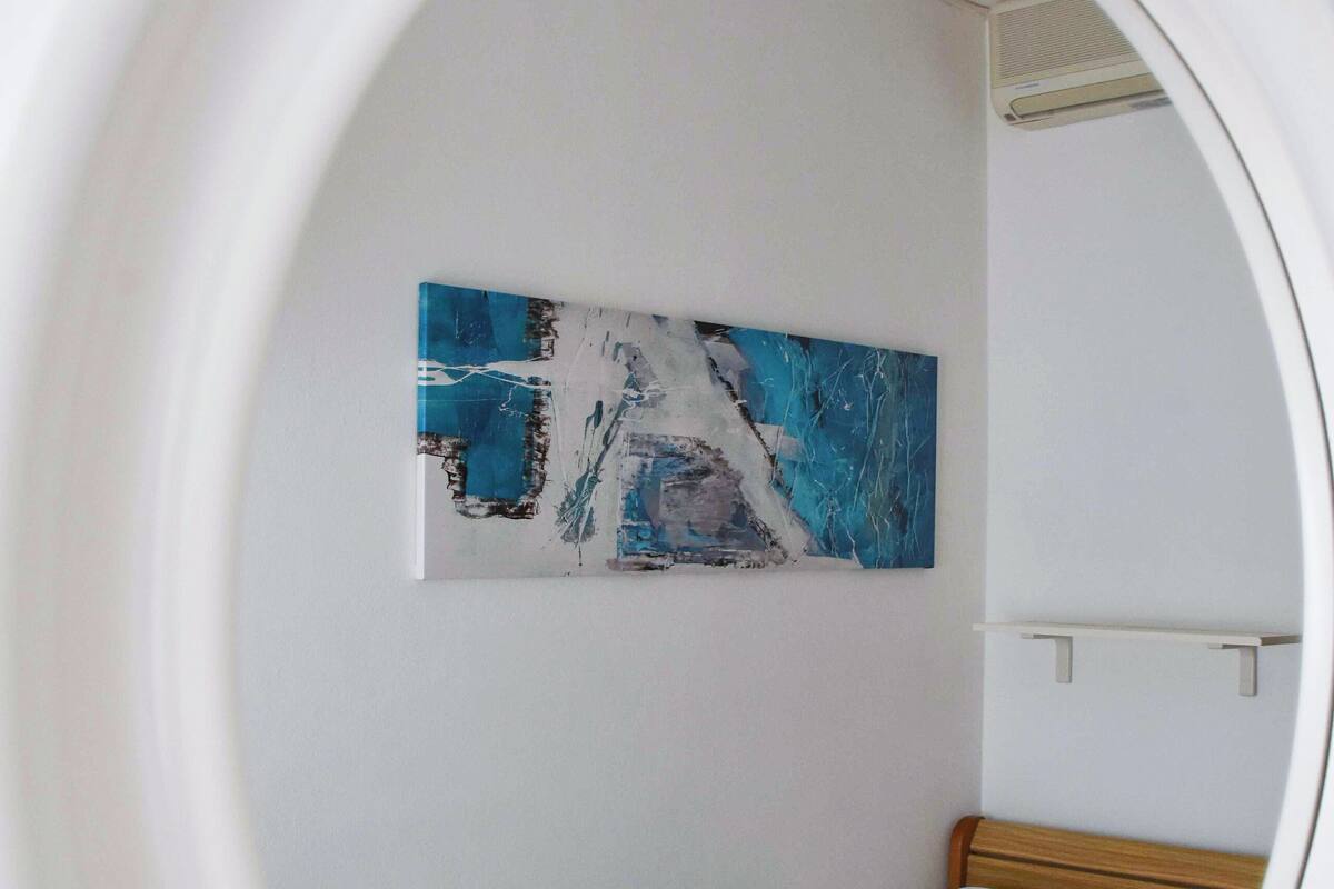 A room with a bed, a painting on the wall, and a window.