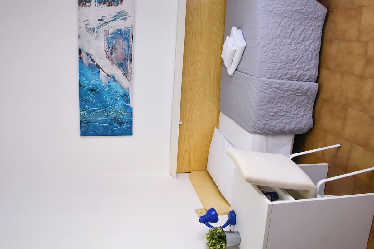 A room with a bed, a painting, a wooden door, and a small desk with a plant.