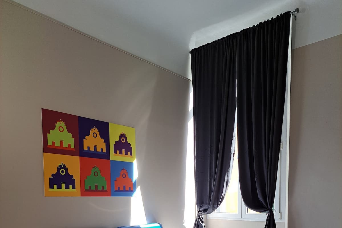 A hotel room with two beds, a colorful wall art piece, a window with dark curtains, and a wooden floor.